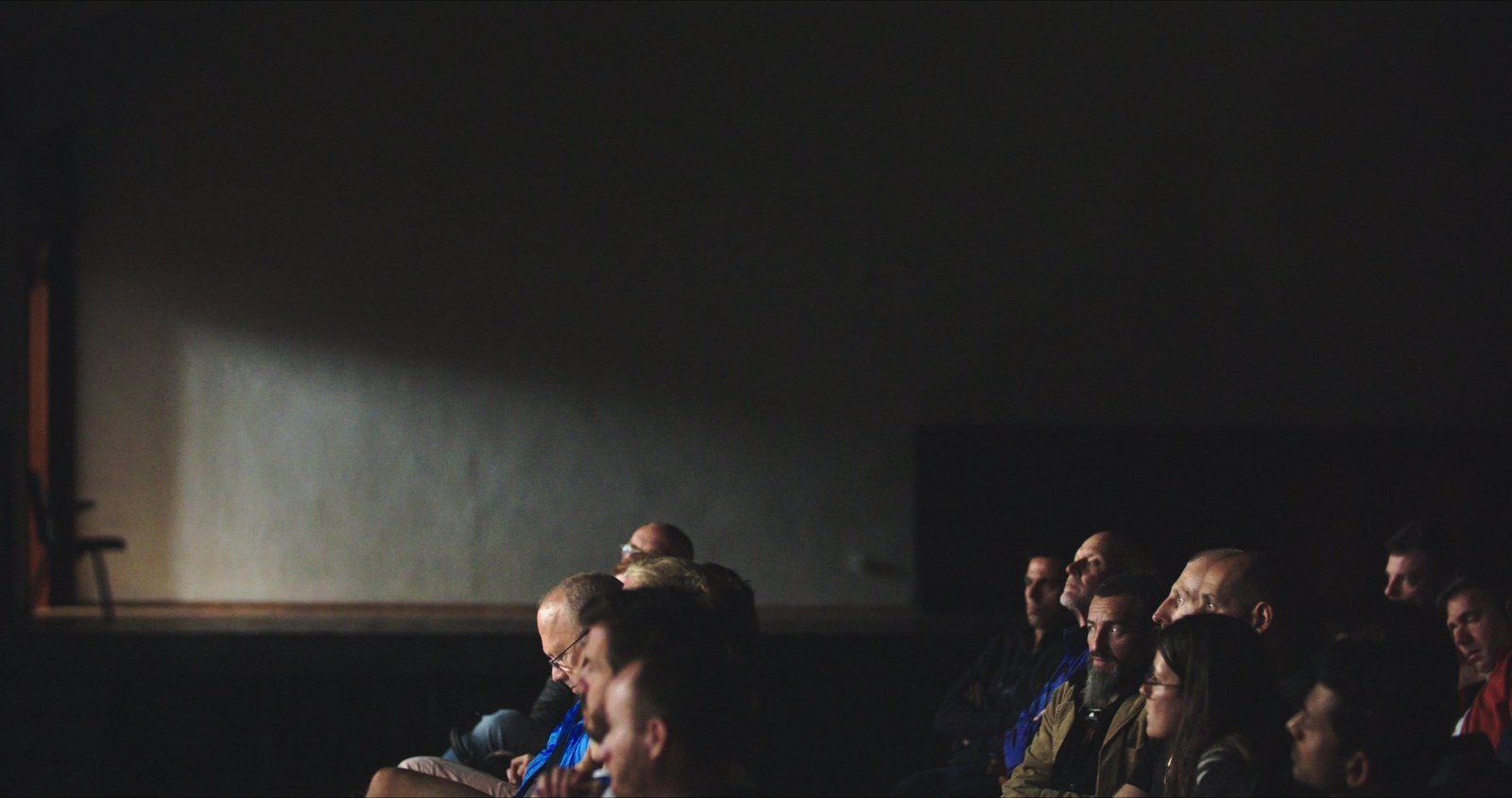 Men and women sit in a dark hall and look in different directions