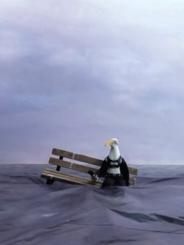 A seagull figure sits on a bench in the sea